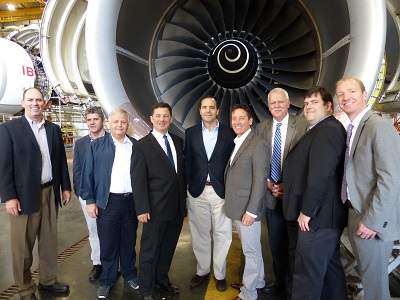 Ten people in front of jet engine under aircraft wing